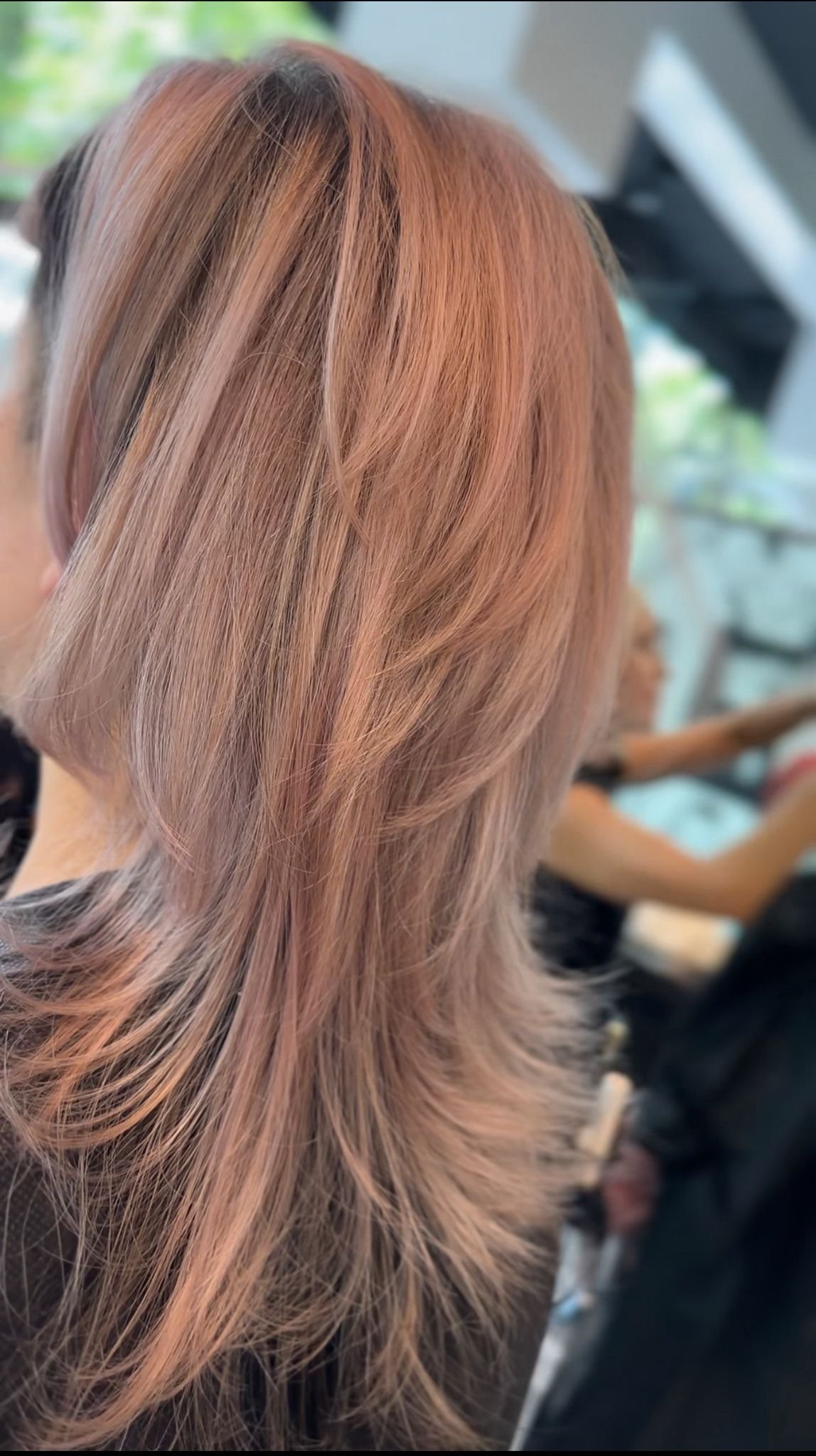 Frau mit welligem, rosafarbenem Haar in einem Friseursalon.