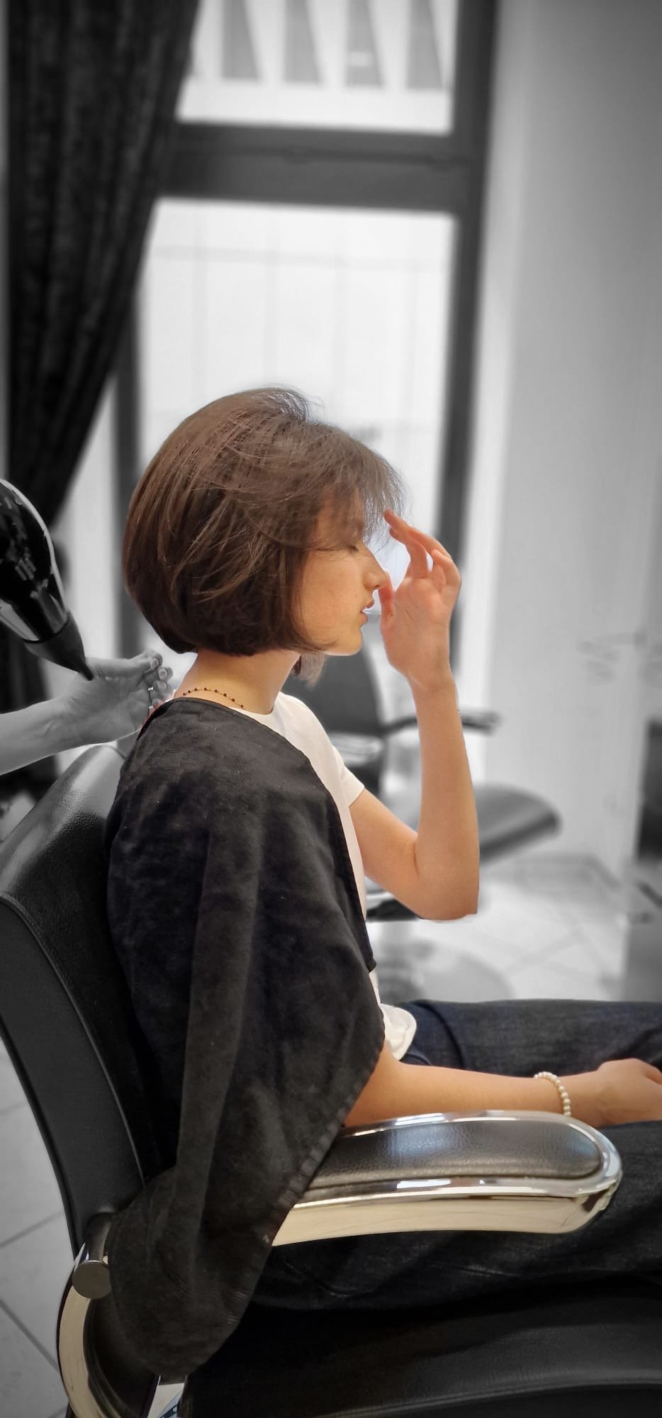 Frau mit Kurzhaarfrisur sitzt im Friseurstuhl, während ihr die Haare trocknet, in einem Friseursalon, im Schwarz-Weiß-Stil mit farbiger Frau